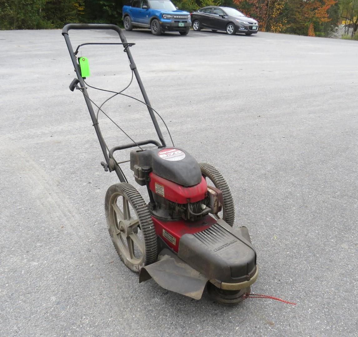 Red and black wheeled string trimmer on asphalt.