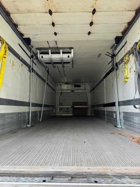 Inside of an empty refrigerated truck with a white interior and a cooling unit on the ceiling.