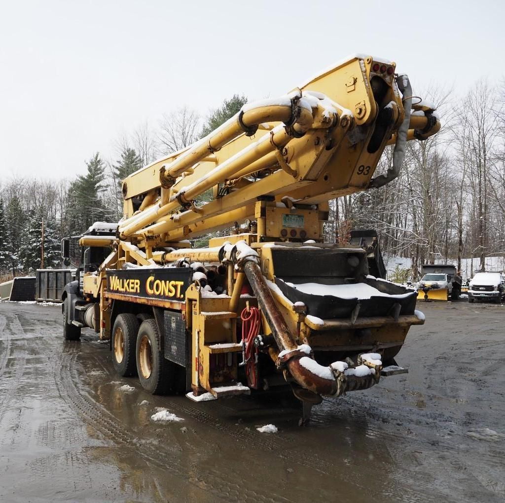 Yellow concrete pump truck in a snowy construction site.