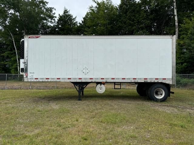 White semi-trailer parked on grass with trees in background.