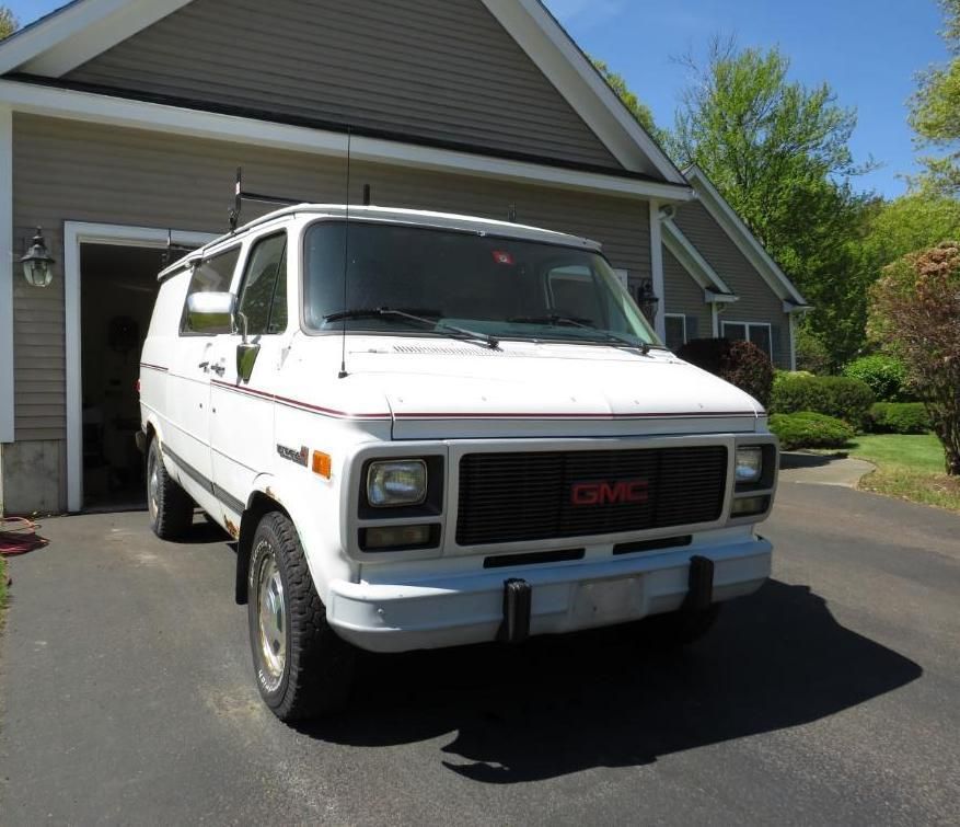 White GMC van parked in front of a garage, black grill, on a sunny day.