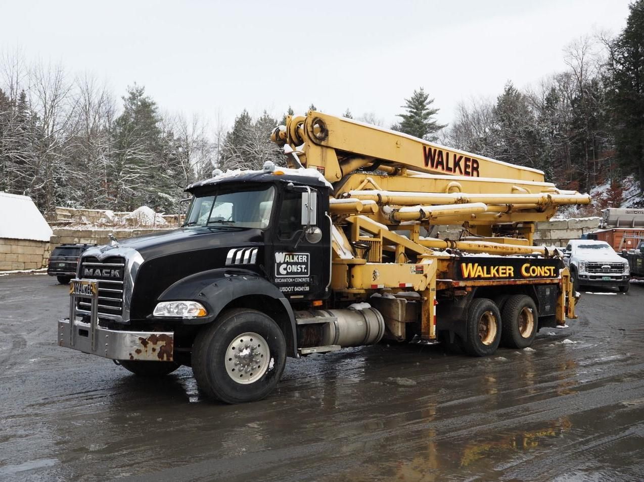 Black and yellow Walker Concrete pump truck in snowy outdoor setting.