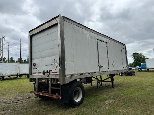 White refrigerated semi-trailer in a grassy field under a cloudy sky.