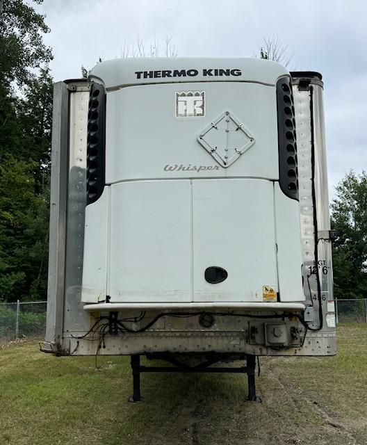 A refrigerated Thermo King trailer parked on grass; gray with black vents, under cloudy sky.