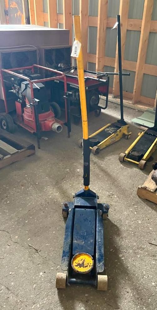Blue and yellow floor jack with a long handle in a garage setting.