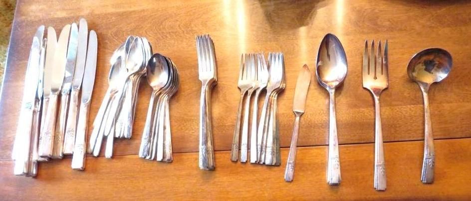 Silverware laid out on a wooden surface, including knives, forks, spoons, and a ladle.