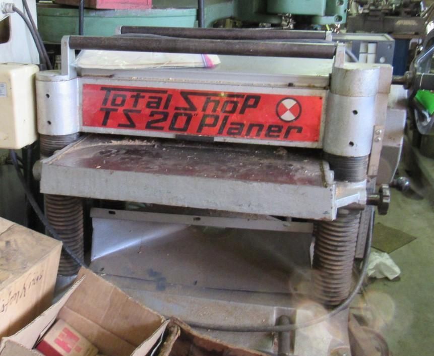 Total Shop TS 20 Planer, a woodworking machine, is in a shop environment. The planer is silver and red.