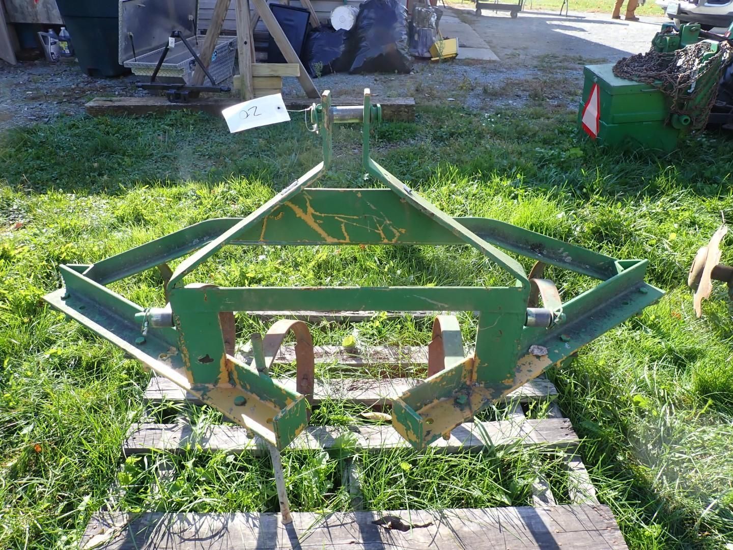 Green metal farm implement on grass, with triangular frame and hitch, outdoors in a yard.