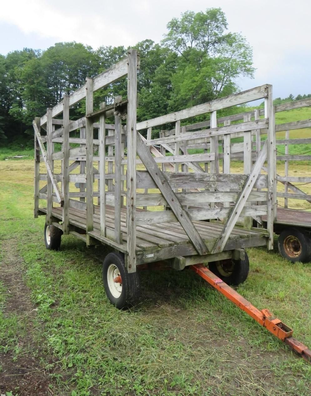 Wooden farm wagon on wheels, with orange tow bar, on a grassy field.