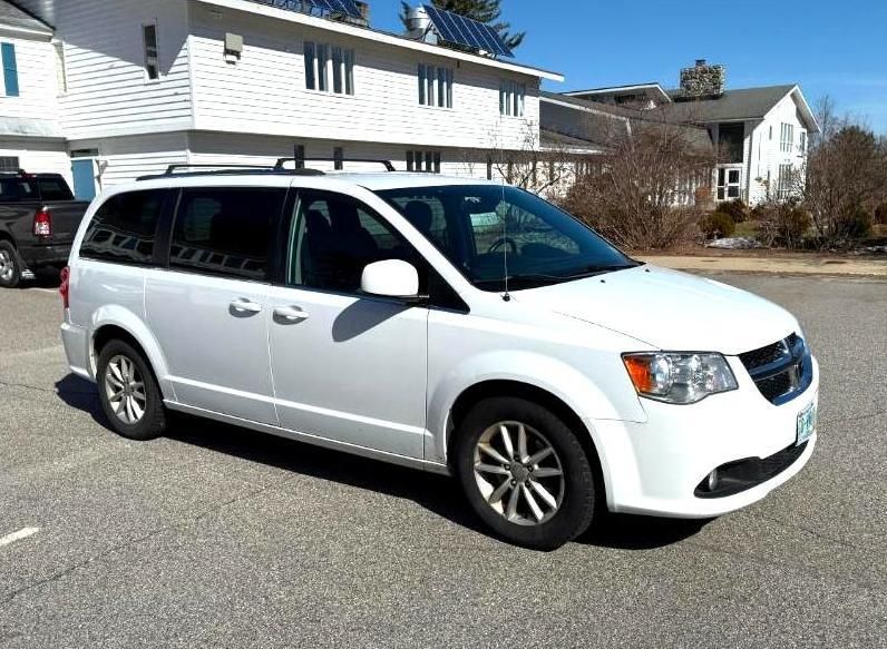 White Dodge Grand Caravan minivan parked in front of a white building on a sunny day.