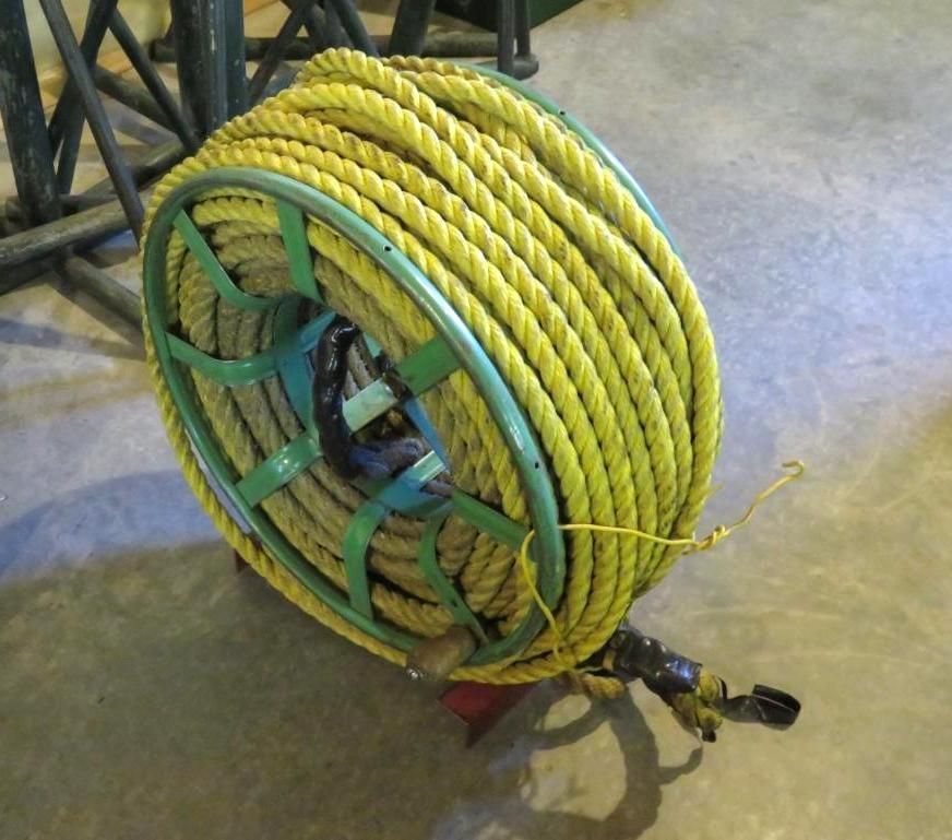 Yellow rope coiled on a green metal reel with a nozzle, sitting on a concrete floor.