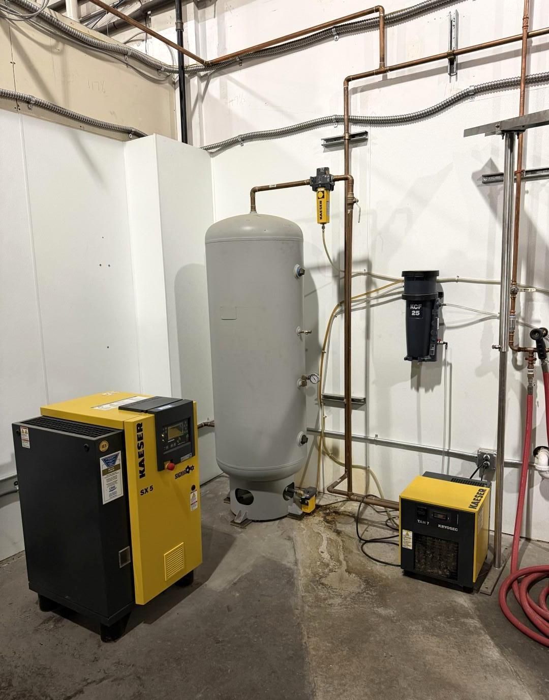 Yellow and black air compressor next to a large, grey tank and other equipment in a utility room.