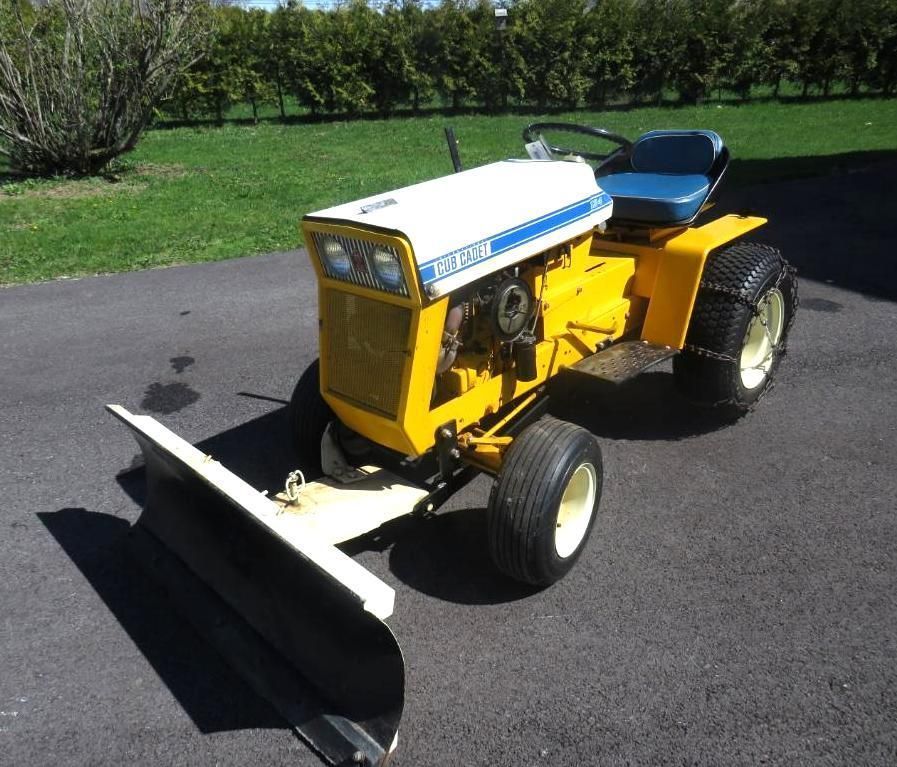 Yellow and white Cub Cadet tractor with snowplow on asphalt driveway.