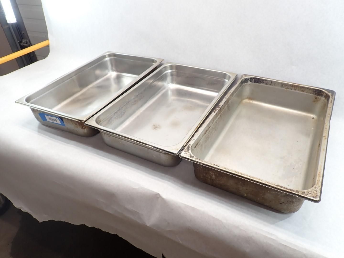 Three stainless steel food pans on a white surface.