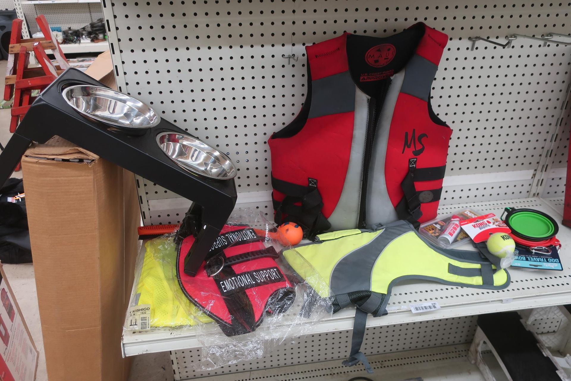 A shelf with a dog bowl stand, life vests, and dog toys in a store.
