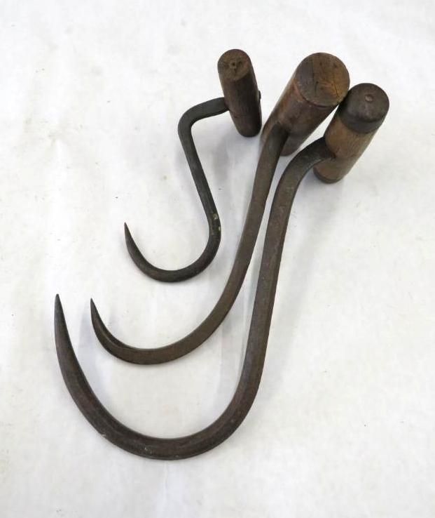 Three metal meat hooks with wooden handles on a white surface.