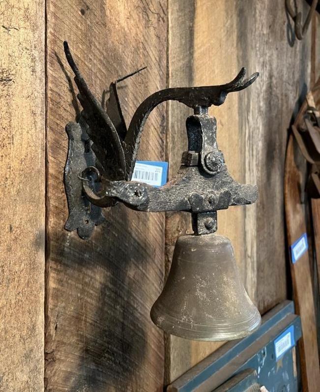 Ornate metal bell mounted on a wooden wall, possibly antique.