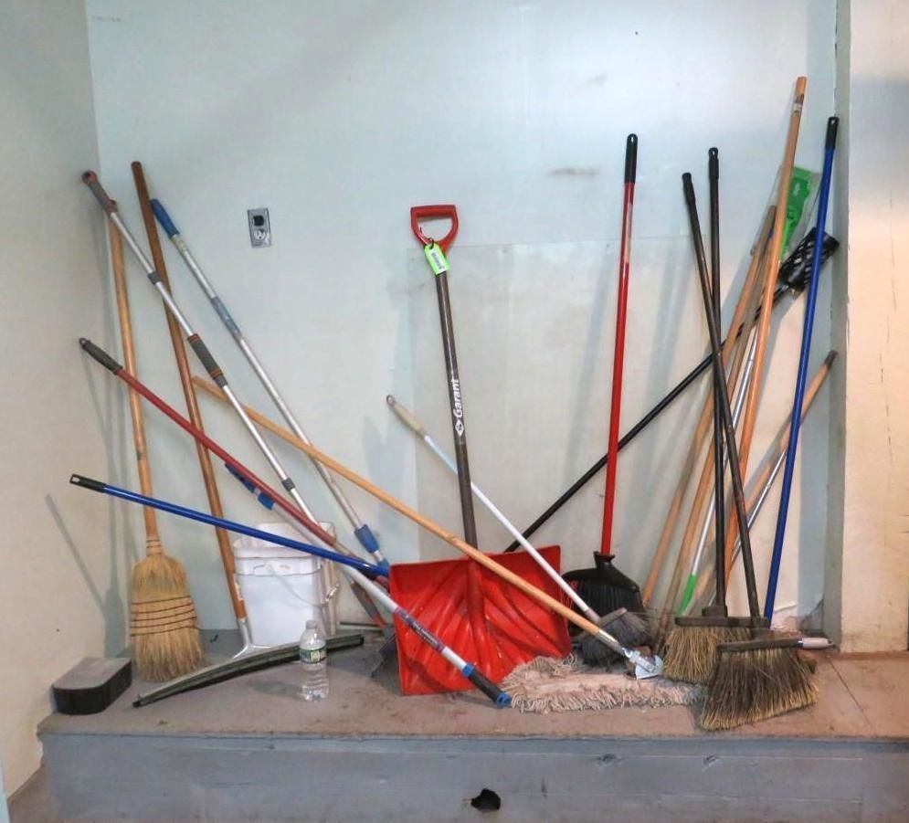 Cleaning tools against a wall: brooms, mops, snow shovel.
