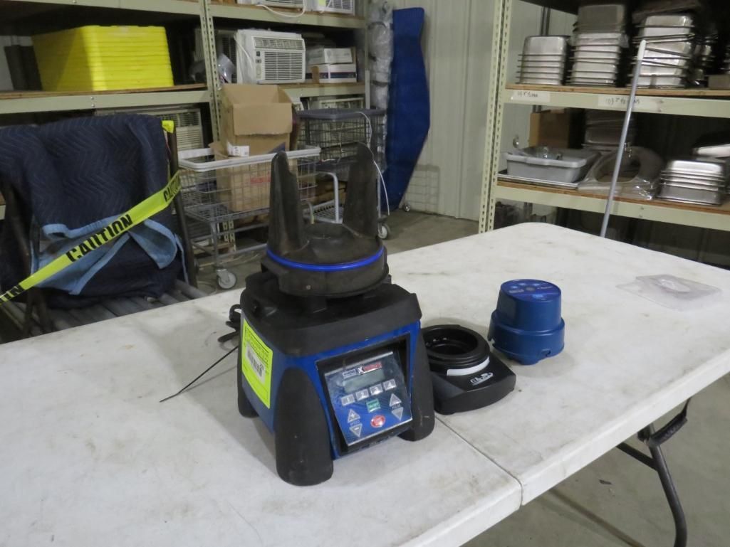 A blue and black laboratory centrifuge on a white table, with a blue container beside it, in a storage room.