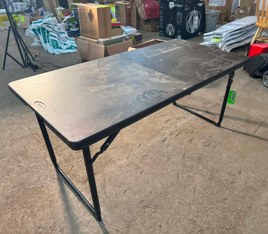 Black folding table with a textured surface, metal legs, in a warehouse setting.
