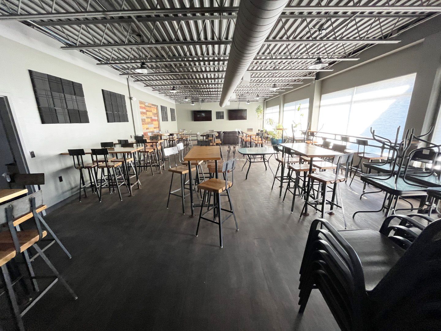 Empty modern venue with tables and chairs, large windows, and an exposed ceiling.