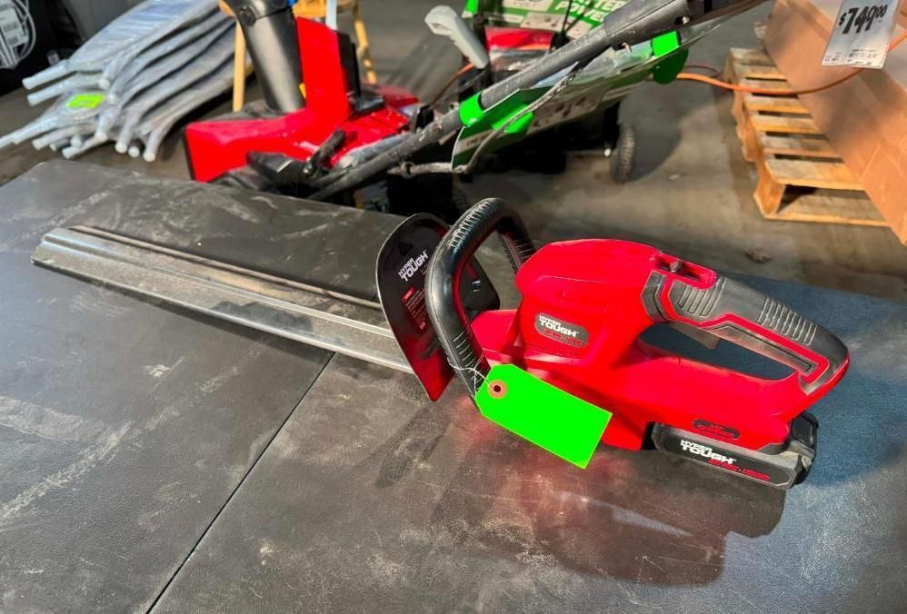 Red and black cordless hedge trimmer on a table with a green price tag.