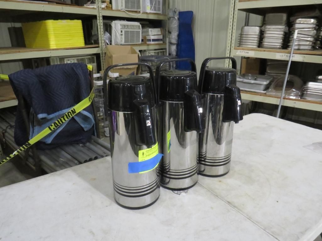 Three stainless steel coffee carafes with black tops on a white surface.