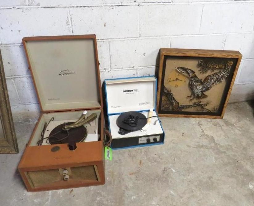 Three vintage record players and an owl art piece on a concrete floor next to a white brick wall.
