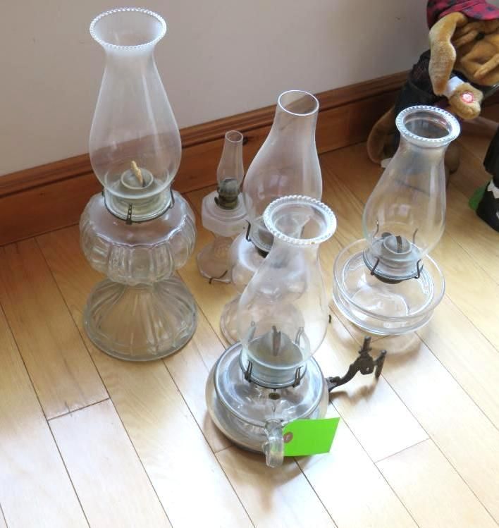 Collection of vintage oil lamps and glass chimneys on a wooden floor.