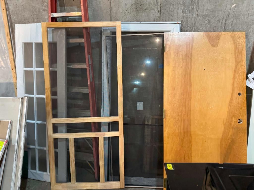 Pile of wooden doors and screen doors leaning against a wall, with a ladder in the background.
