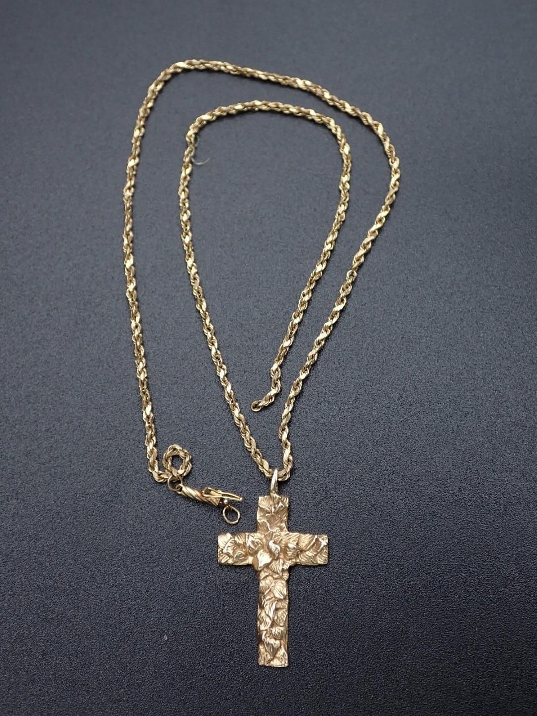 Gold necklace with a textured cross pendant on a dark surface.