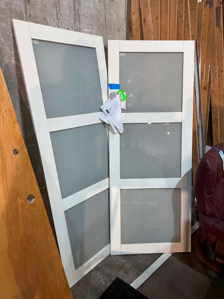 Two white-framed doors with frosted glass panels leaning against a wall.