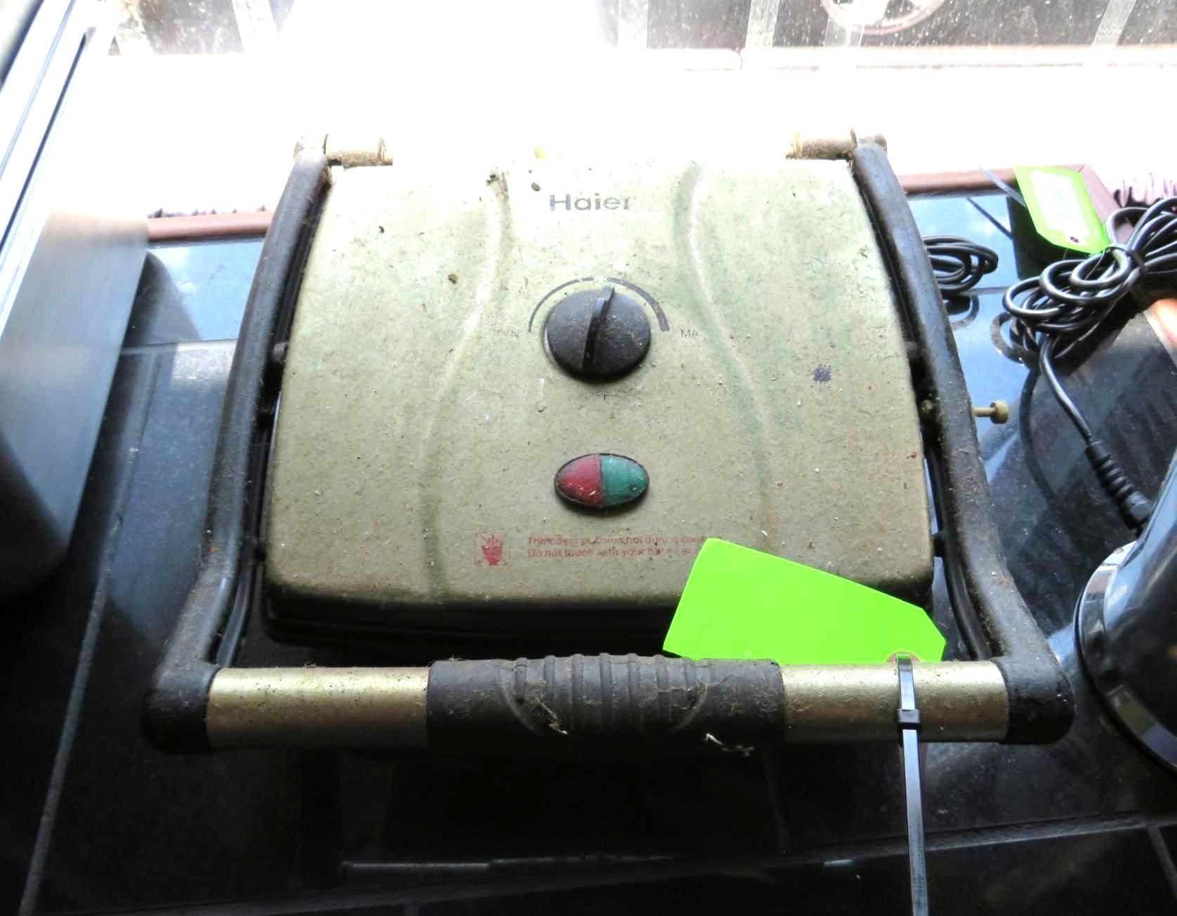A used, gold panini press with a black handle and a green and red light.