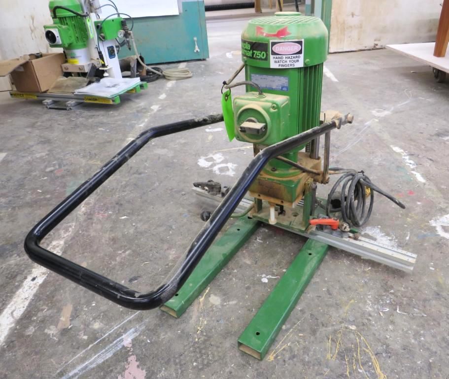 Green mortise machine with black handle in a workshop.