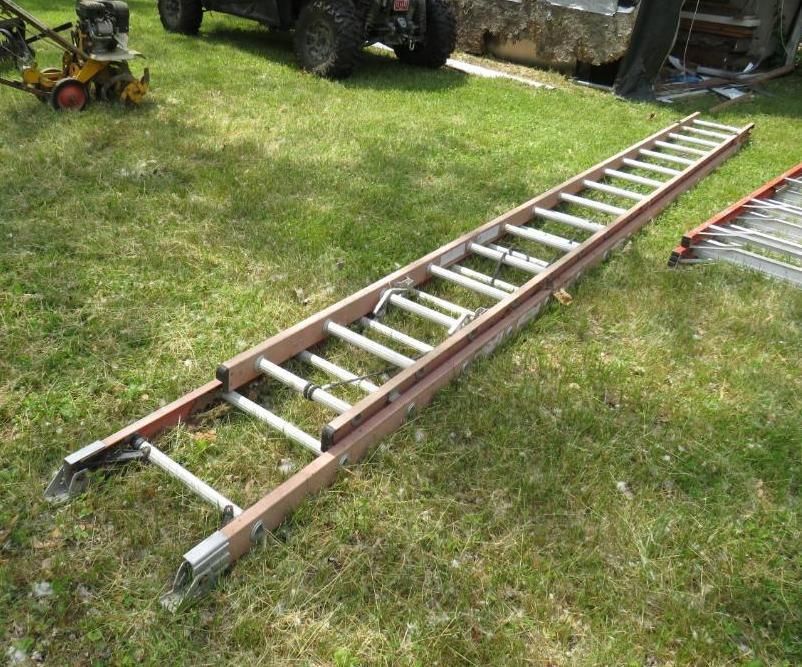 Long, brown and silver extension ladder lying on green grass.
