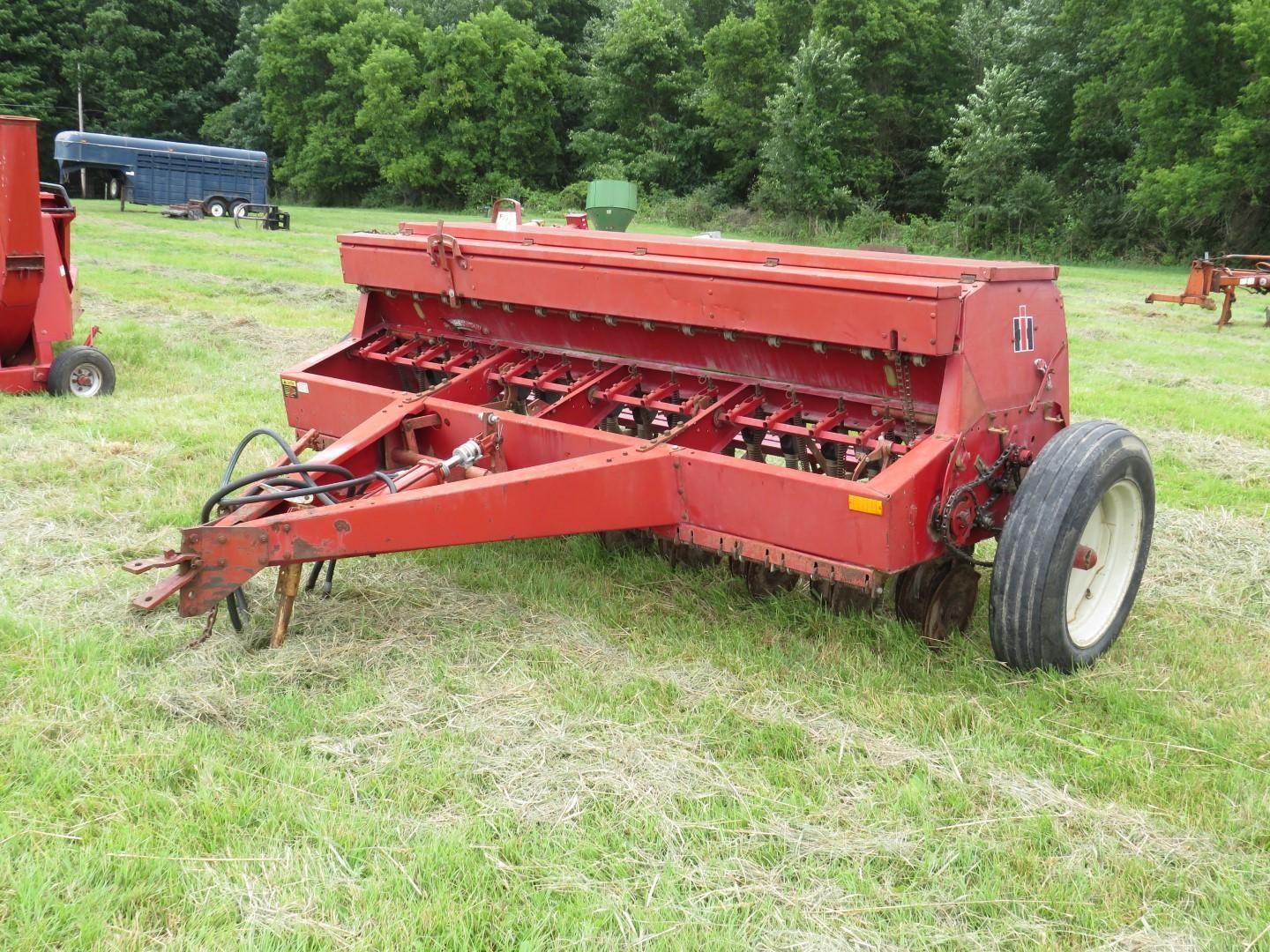 Red farm grain drill machine in a grassy field.