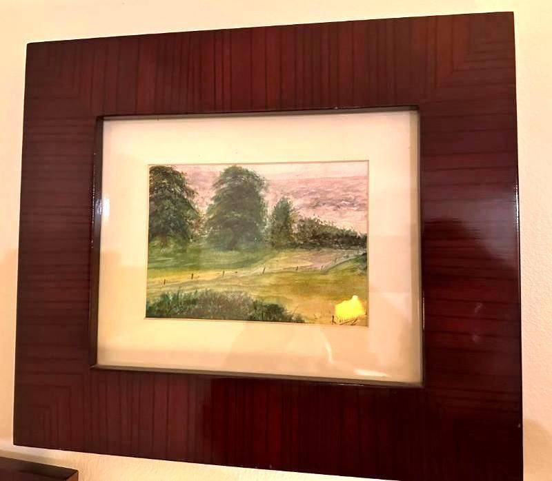 Watercolor landscape painting in a glossy, dark wood frame, featuring trees, a field, and a sky.