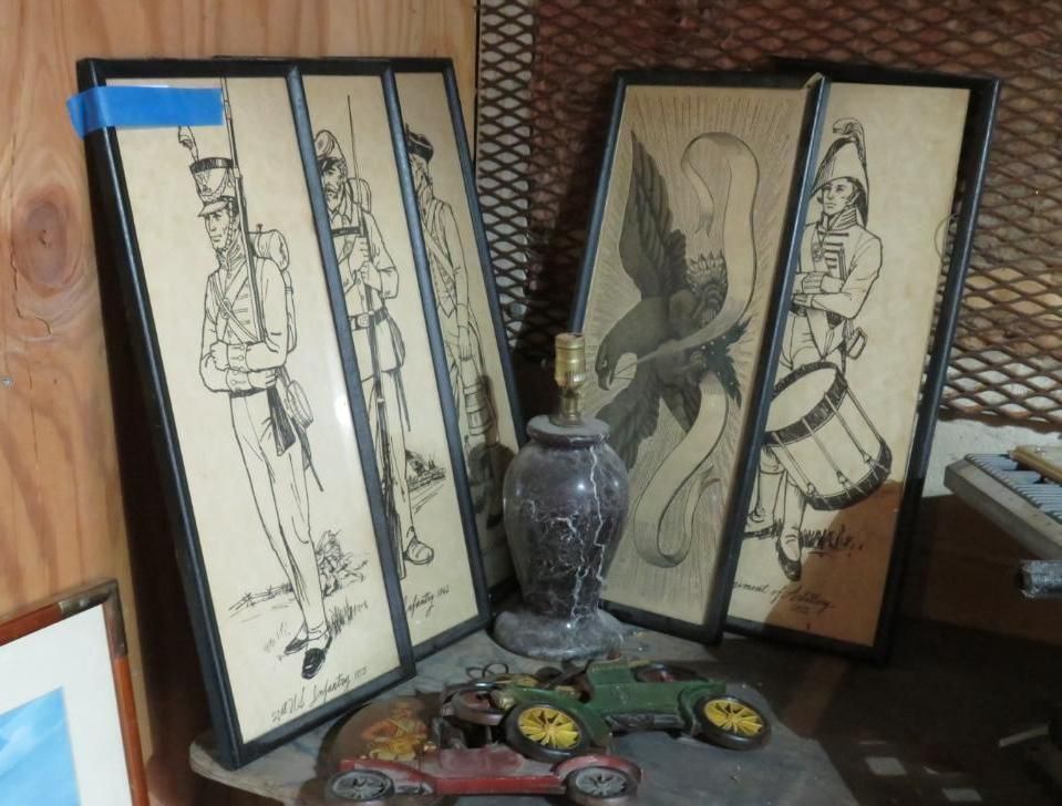 Four framed drawings, two with soldier figures, one with an eagle, and one with a drum player, with a lamp and toy cars.