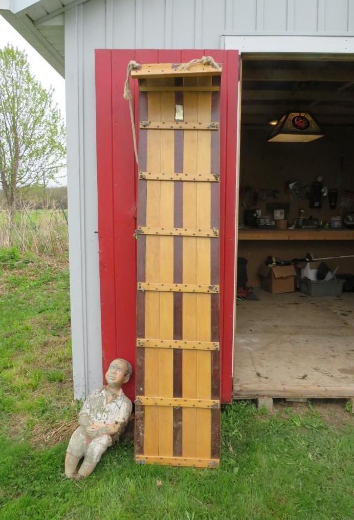 Wooden sled propped against a red shed door, with a stone statue of a person on the ground.