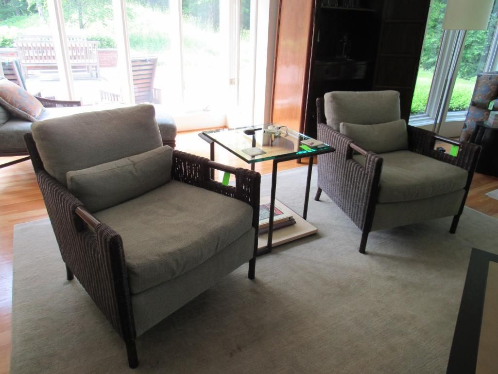Two gray cushioned armchairs in a living room, next to a small glass-topped table and a window.