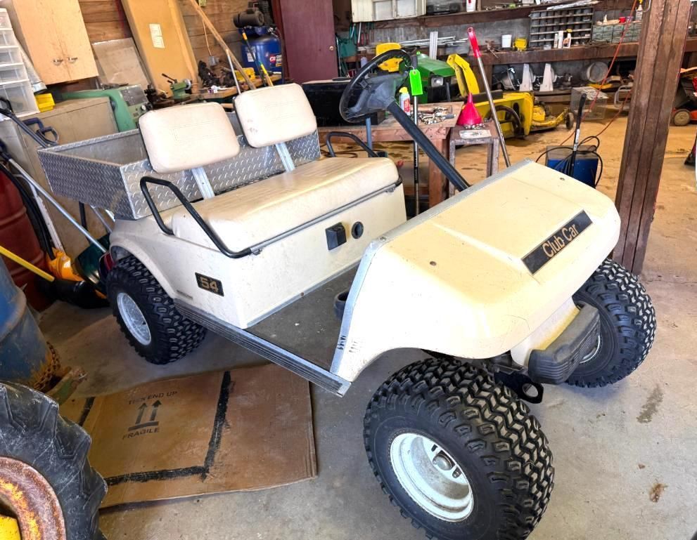 Beige Club Car utility vehicle with cargo bed, off-road tires, parked in a garage.