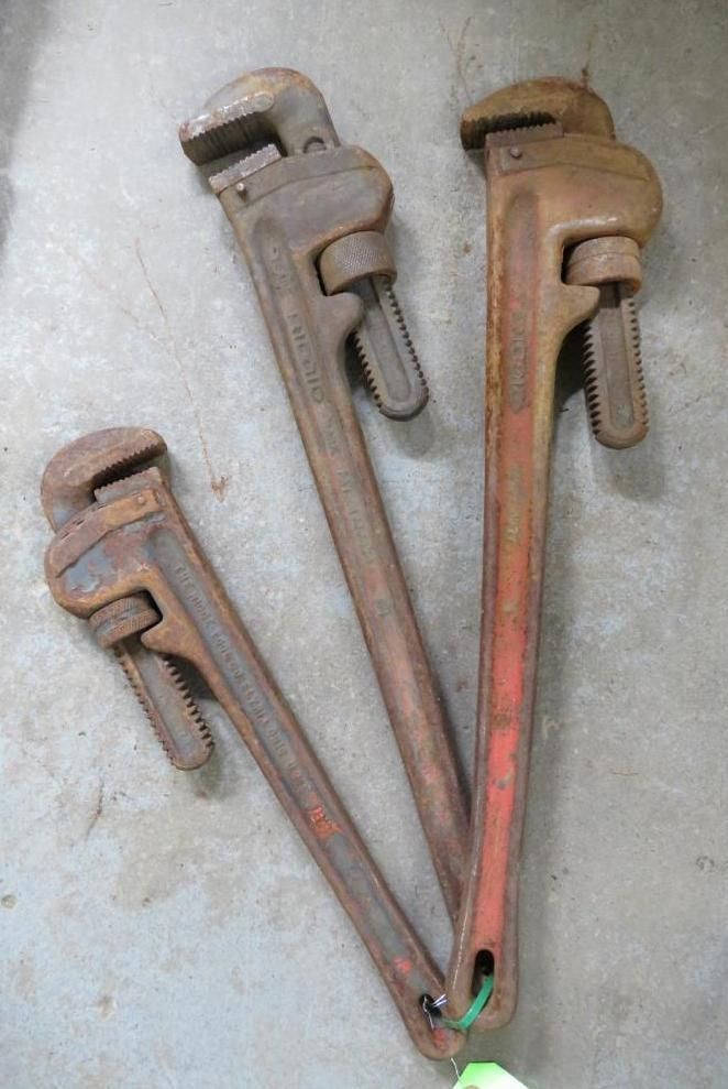 Three pipe wrenches of varying sizes lie on a surface.