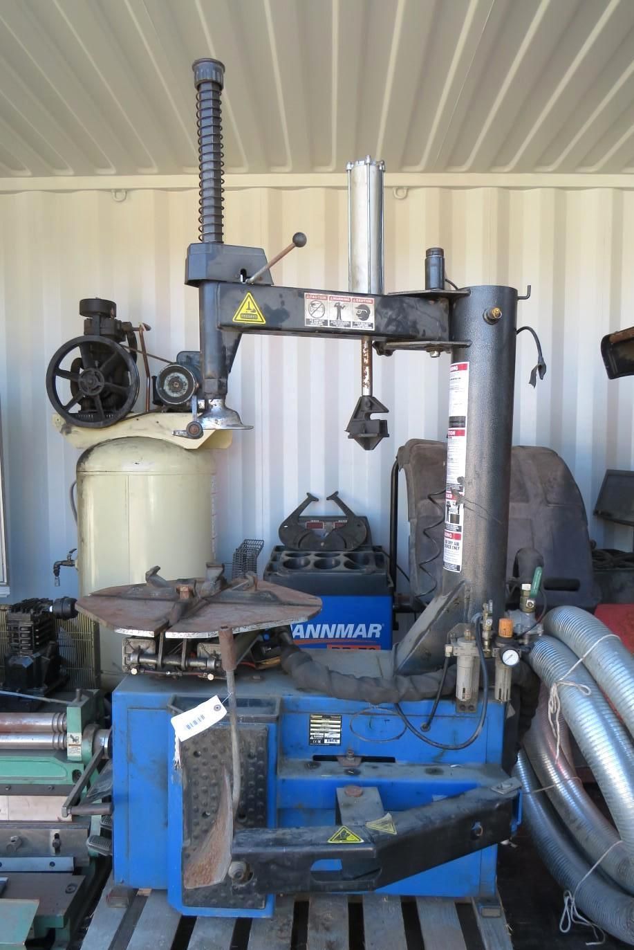 Blue and black tire changing machine with a vertical arm, inside a container.