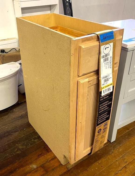 Unfinished kitchen cabinet with a drawer and a door, with packaging tag attached.