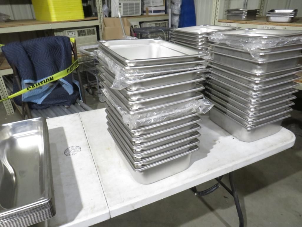 Stacks of stainless steel food trays on a white folding table.