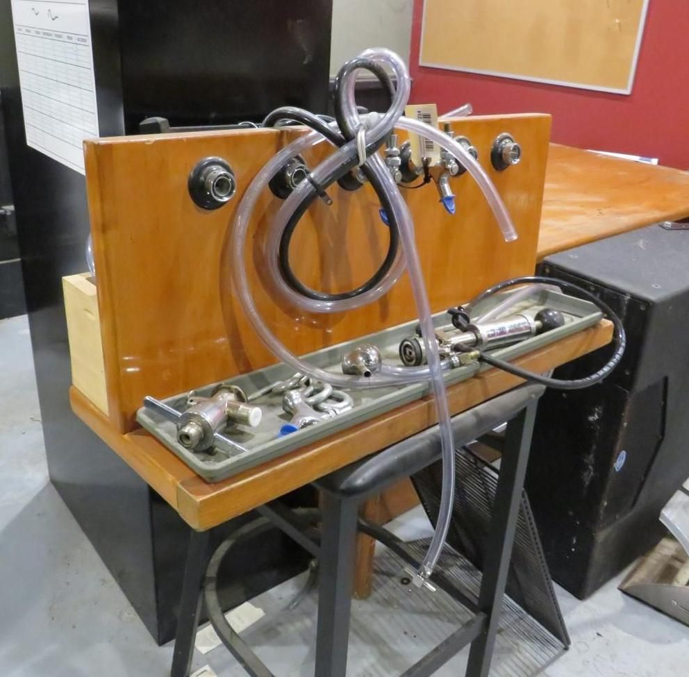 A wooden draft beer tap setup with hoses and hardware on a stool in a workshop.