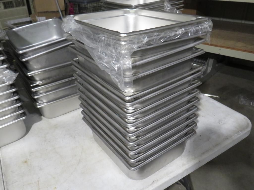 Stack of stainless steel food pans on a white table, ready for use.