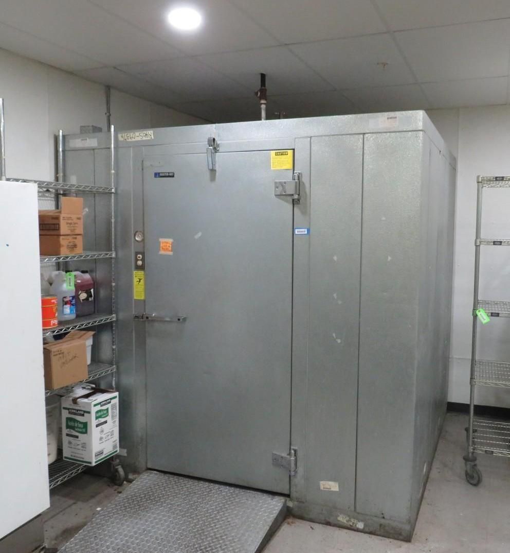 Large walk-in refrigerator in a commercial kitchen, gray metal exterior, metal shelving on the left.