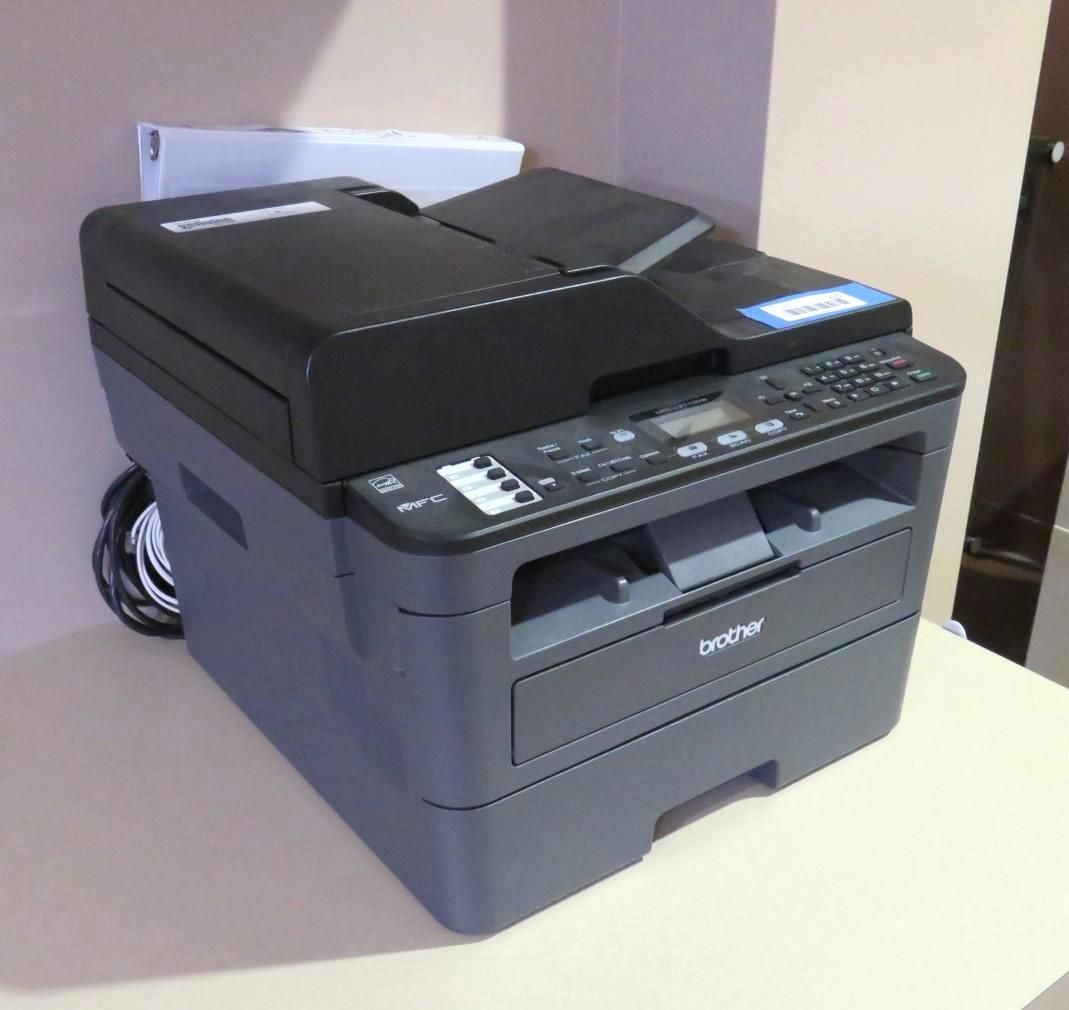 Brother black and gray all-in-one printer on a light surface against a cream-colored wall.