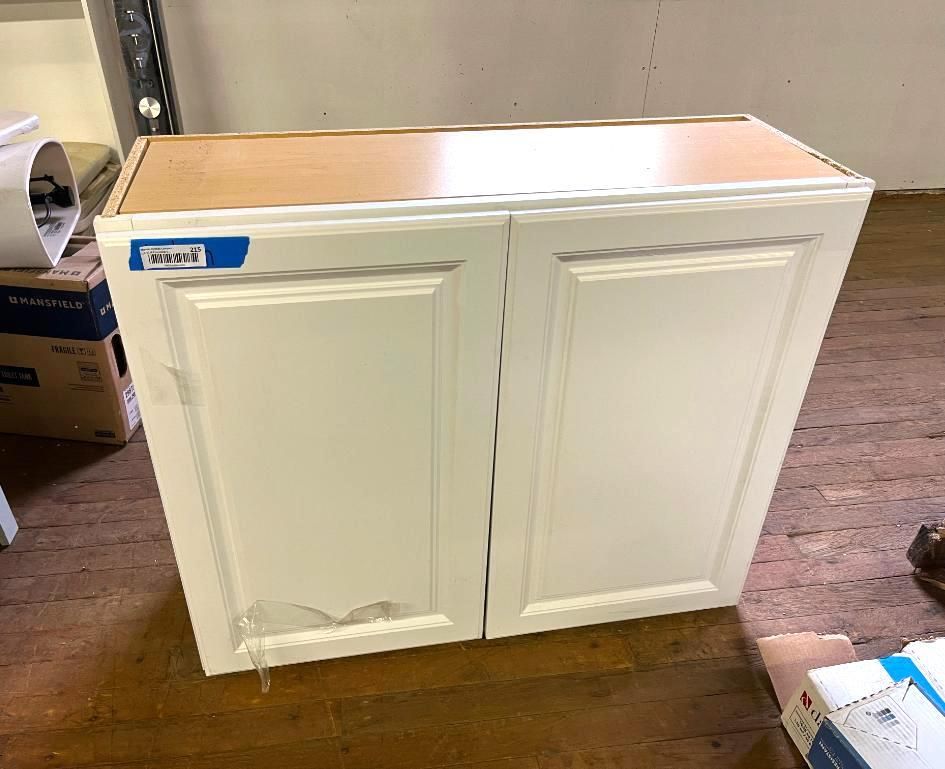 White two-door kitchen cabinet with a light wood top. Cabinet is on a wooden floor.
